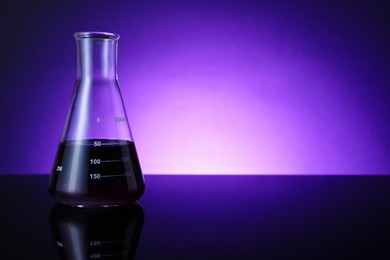 Photo of Flask with color liquid on table against violet background. Space for text