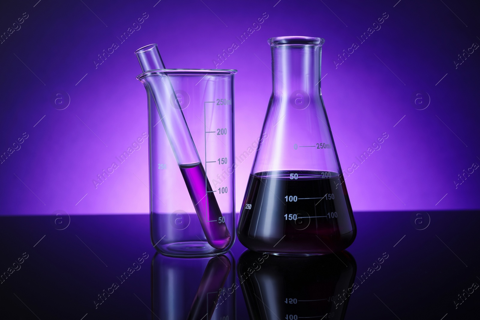 Photo of Different laboratory glassware with color liquid on table against violet background