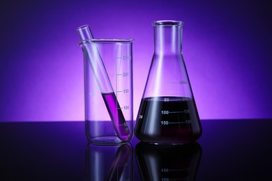 Photo of Different laboratory glassware with color liquid on table against violet background