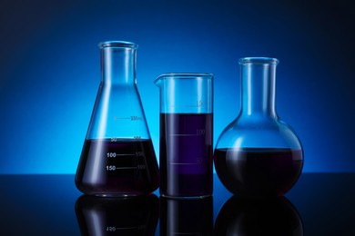 Photo of Different laboratory glassware with color liquid on table against blue background