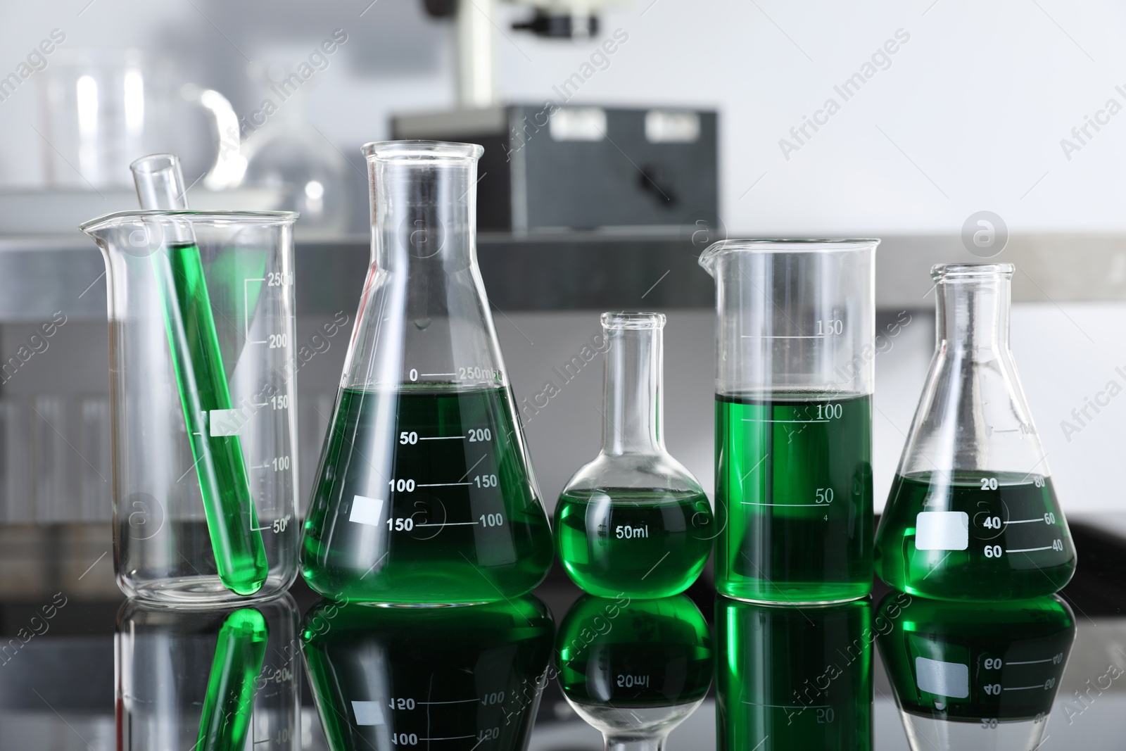 Photo of Different glassware with green liquid on table in laboratory, closeup