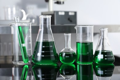 Photo of Different glassware with green liquid on table in laboratory, closeup