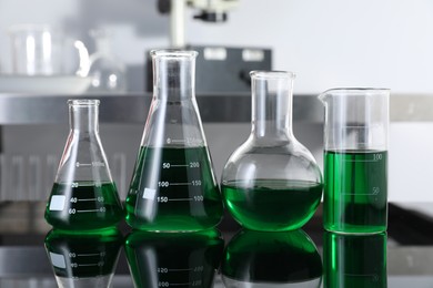 Photo of Different glassware with green liquid on table in laboratory, closeup