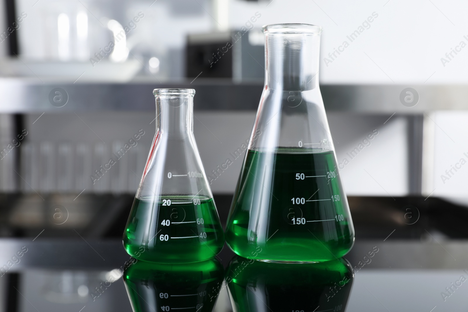 Photo of Glass flasks with green liquid on table in laboratory, closeup
