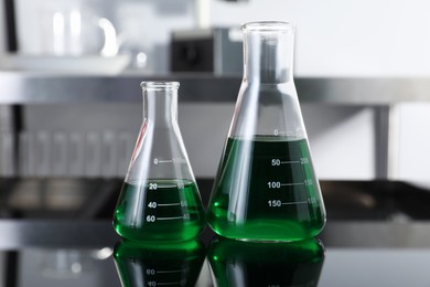 Photo of Glass flasks with green liquid on table in laboratory, closeup