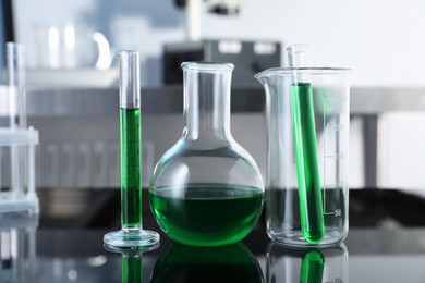 Photo of Different glassware with green liquid on table in laboratory, closeup