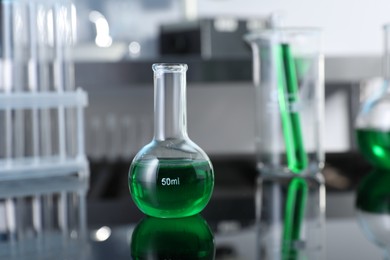 Photo of Glass flask and other glassware with green liquid on table in laboratory, closeup