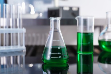 Photo of Glass flask and other glassware with green liquid on table in laboratory, closeup