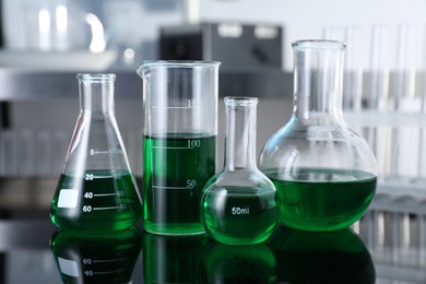 Photo of Different glassware with green liquid on table in laboratory, closeup