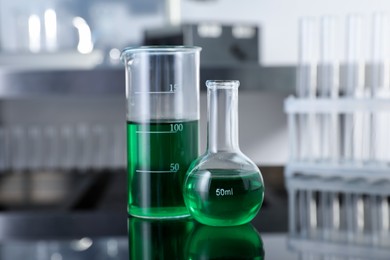 Photo of Glass beaker and flask with green liquid on table in laboratory, closeup