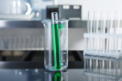 Photo of Glass beaker and test tube with green liquid on table in laboratory, closeup