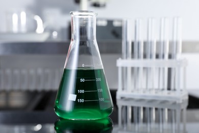 Photo of Glass flask with green liquid on table in laboratory, closeup