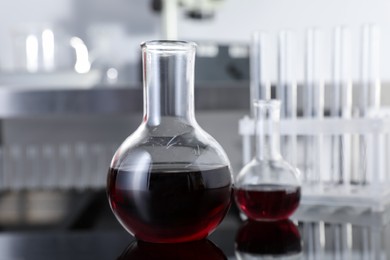 Photo of Glass flasks with red liquid on table in laboratory, closeup