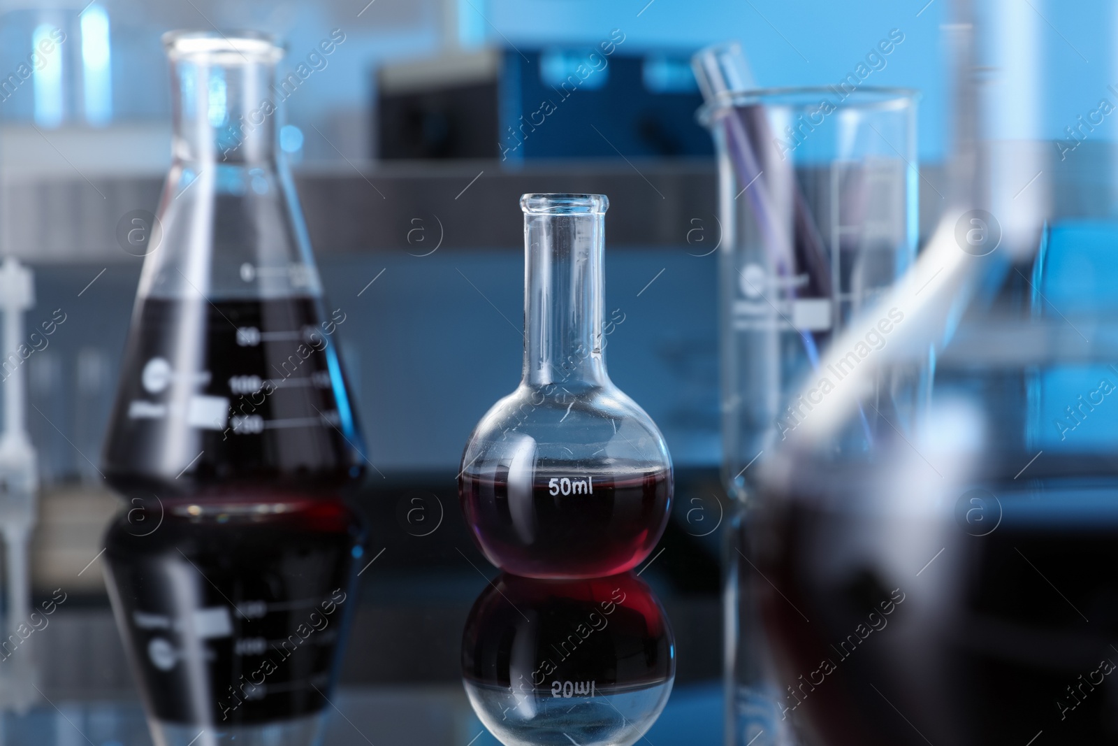 Photo of Different glassware with red liquid on table in laboratory, selective focus