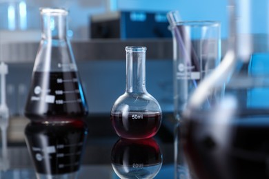 Photo of Different glassware with red liquid on table in laboratory, selective focus