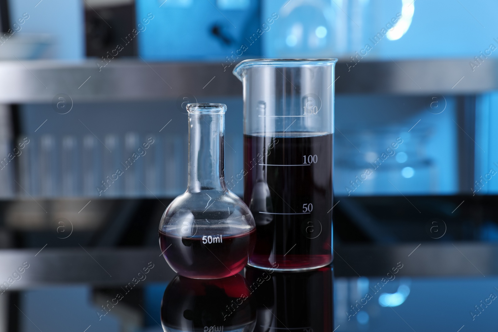 Photo of Glass beaker and flask with red liquid on table in laboratory, closeup