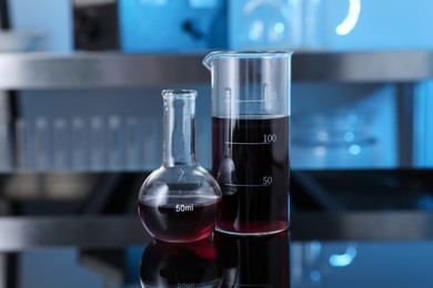 Photo of Glass beaker and flask with red liquid on table in laboratory, closeup