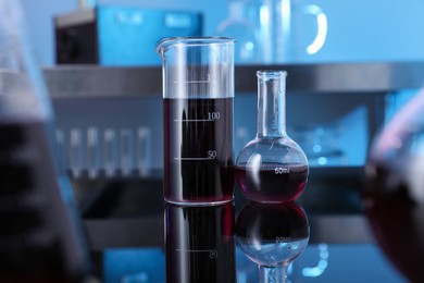 Photo of Glass beaker and flask with red liquid on table in laboratory, selective focus