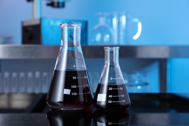 Photo of Glass flasks with red liquid on table in laboratory, closeup
