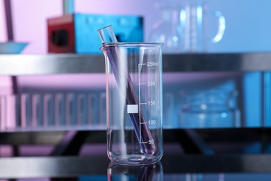 Photo of Glass beaker and test tube with red liquid on table in laboratory, closeup