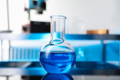 Photo of Glass flask with blue liquid on table in laboratory, closeup