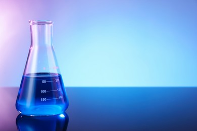 Photo of Glass flask with blue liquid on mirror surface against color background, space for text