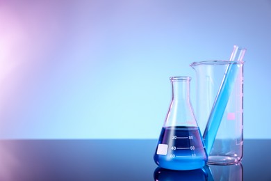 Photo of Different glassware with blue liquid on mirror surface against color background, space for text