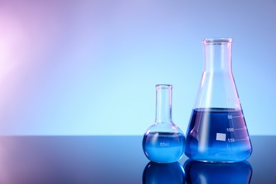 Photo of Glass flasks with blue liquid on mirror surface against color background, space for text