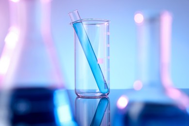 Photo of Different glassware with blue liquid on mirror surface against color background