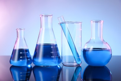 Photo of Different glassware with blue liquid on mirror surface against color background