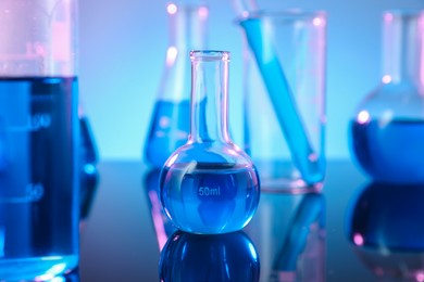 Photo of Different glassware with blue liquid on mirror surface against color background