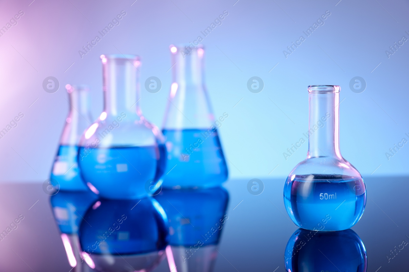 Photo of Different glassware with blue liquid on mirror surface against color background
