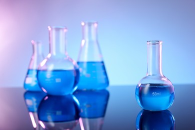 Photo of Different glassware with blue liquid on mirror surface against color background