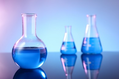 Photo of Different glassware with blue liquid on mirror surface against color background