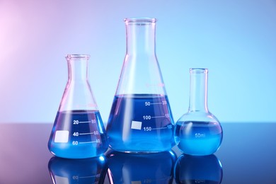 Photo of Glass flasks with blue liquid on mirror surface against color background