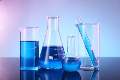 Photo of Different glassware with blue liquid on mirror surface against color background