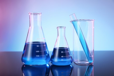 Photo of Different glassware with blue liquid on mirror surface against color background