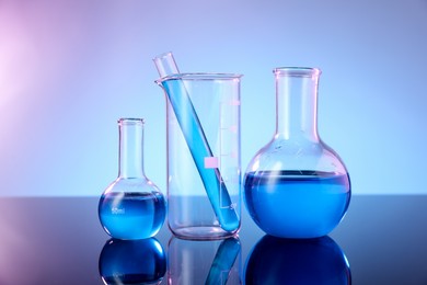 Photo of Different glassware with blue liquid on mirror surface against color background