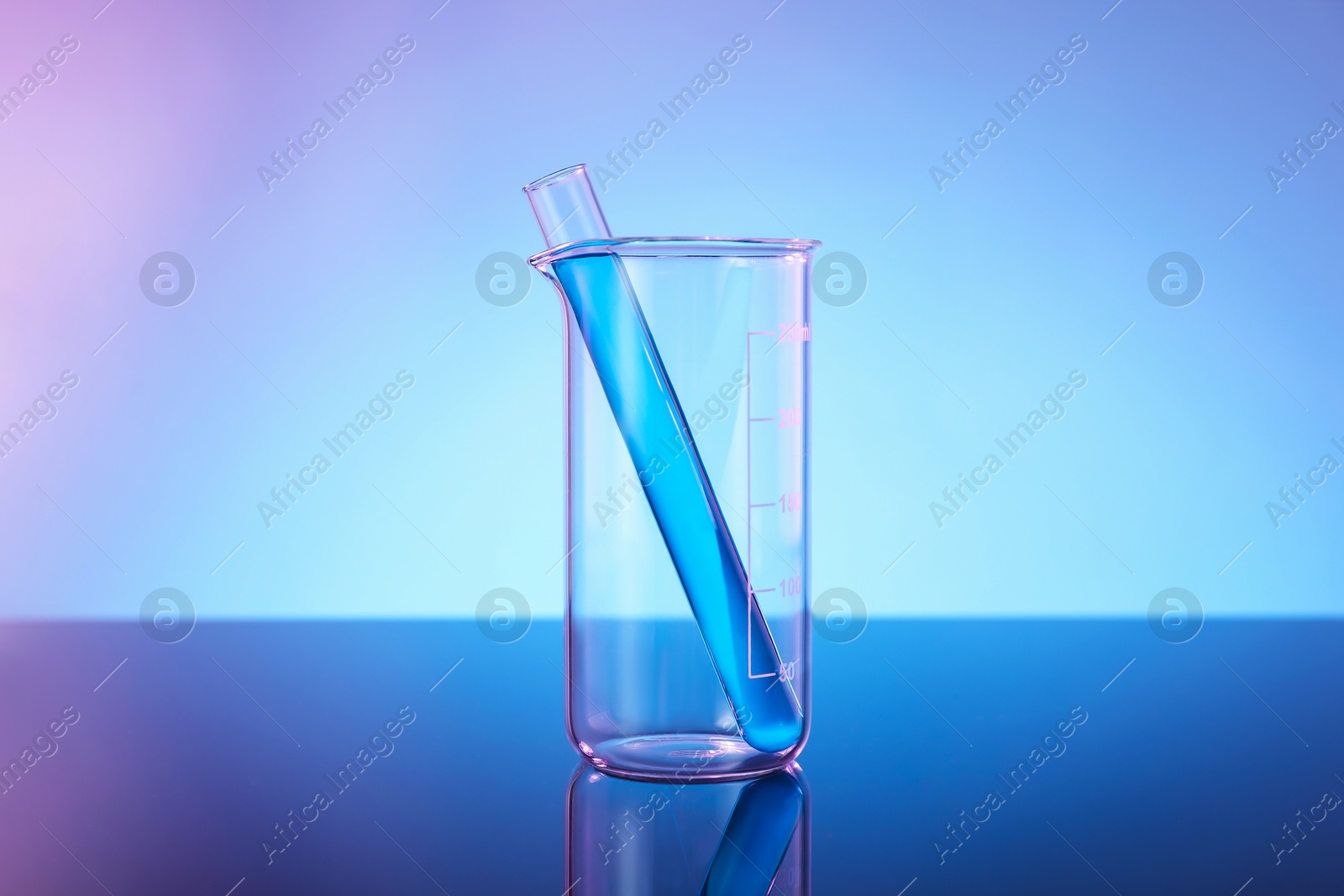 Photo of Glass beaker and test tube with blue liquid on mirror surface against color background