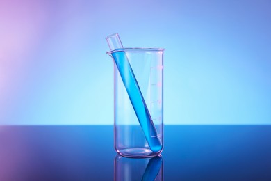 Photo of Glass beaker and test tube with blue liquid on mirror surface against color background