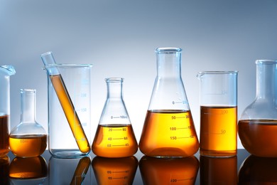 Photo of Different glassware with orange liquid on mirror surface against grey background