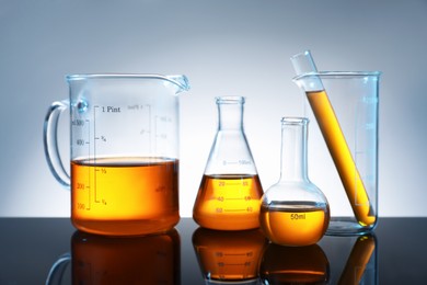 Photo of Different glassware with orange liquid on mirror surface against grey background