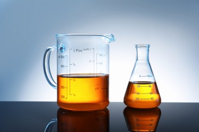 Photo of Glass flask and beaker with orange liquid on mirror surface against grey background