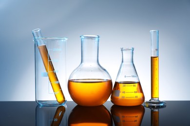 Photo of Different glassware with orange liquid on mirror surface against grey background