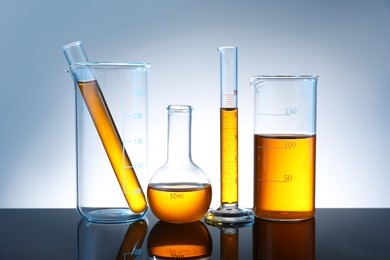 Photo of Different glassware with orange liquid on mirror surface against grey background