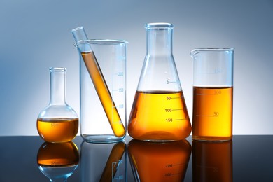 Photo of Different glassware with orange liquid on mirror surface against grey background