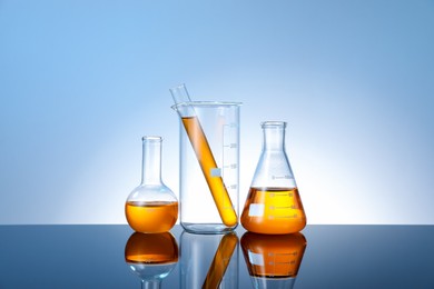 Photo of Different glassware with orange liquid on mirror surface against light blue background