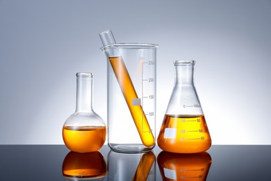 Photo of Different glassware with orange liquid on mirror surface against grey background