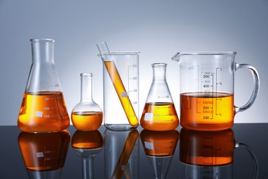Photo of Different glassware with orange liquid on mirror surface against grey background