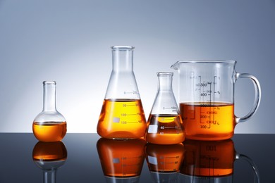 Photo of Different glassware with orange liquid on mirror surface against grey background